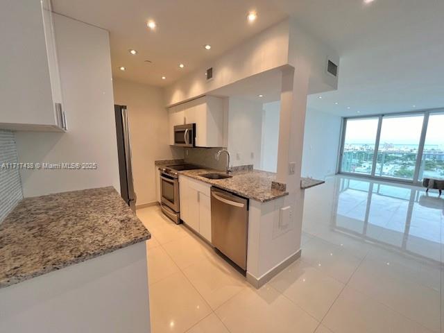 A modern kitchen with granite countertops, stainless steel appliances, and white cabinets overlooks a living area — 1000 West Ave # 07, Miami Beach FL 33139, MIAMI BEACH, FL