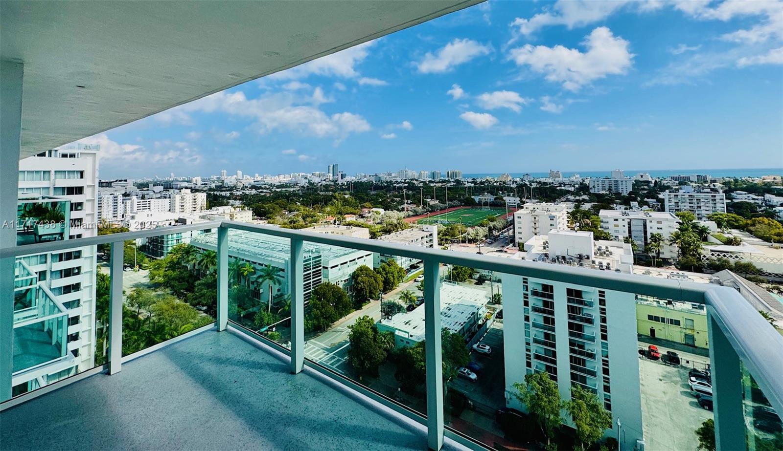 A high-rise balcony overlooks a city landscape with a sports field and the ocean beyond — 1000 West Ave # 07, Miami Beach FL 33139, MIAMI BEACH, FL