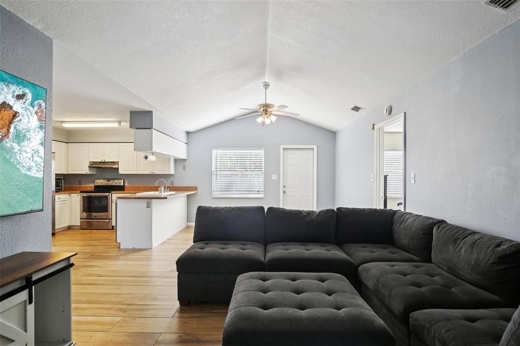 A living room with a vaulted ceiling, dark sectional sofa, and an open-concept kitchen — 3501 W REYNOLDS STREET, PLANT CITY, FL