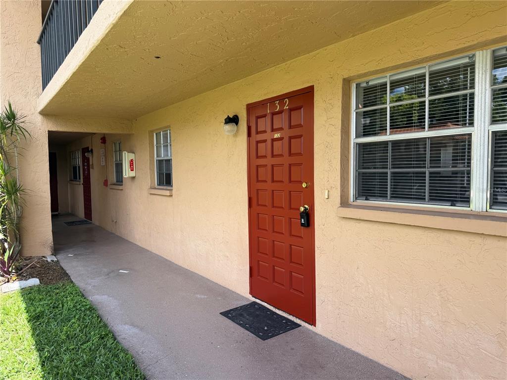 A red front door with the number 132 is set in a tan stucco exterior wall — 4500 E BAY DRIVE UNIT 132, CLEARWATER, FL