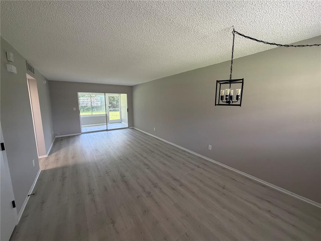 An empty living room features light wood-look flooring, gray walls, and a hanging metal chandelier — 4500 E BAY DRIVE UNIT 132, CLEARWATER, FL