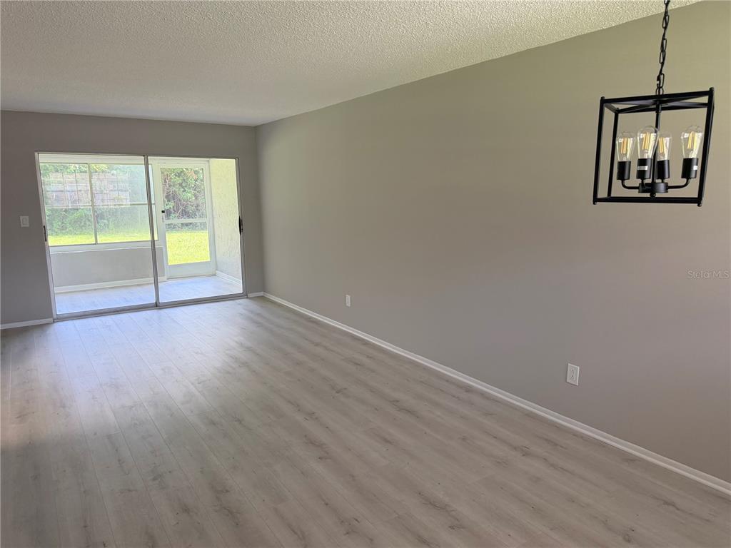 An empty room features light wood-look flooring, gray walls, a modern chandelier, and sliding glass doors — 4500 E BAY DRIVE UNIT 132, CLEARWATER, FL