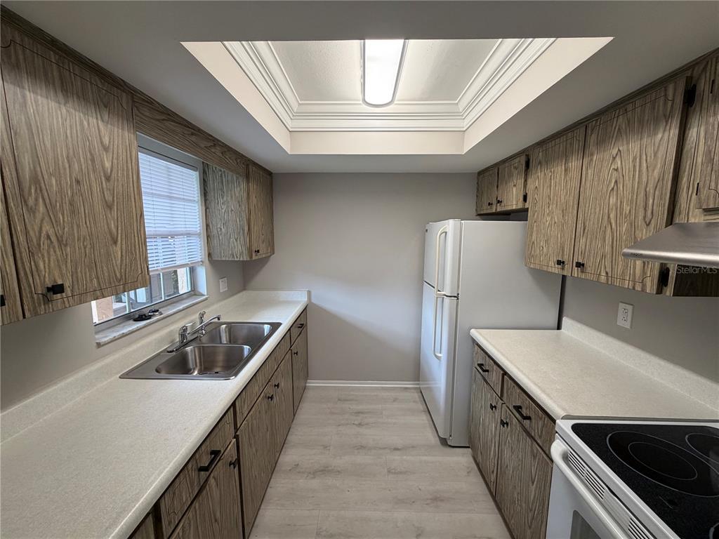 A galley kitchen features wood-grain cabinets, white countertops, a skylight, and light-colored wood flooring — 4500 E BAY DRIVE UNIT 132, CLEARWATER, FL