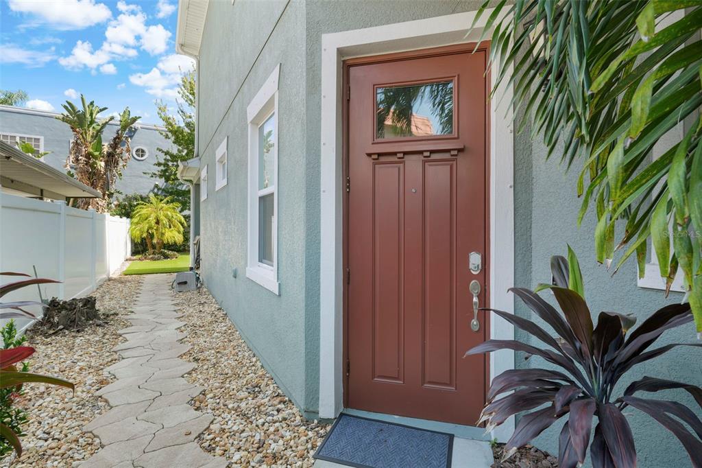 A side entrance with a brown door, a stone walkway, and a white privacy fence — 214 S HABANA AVENUE UNIT 1, TAMPA, FL