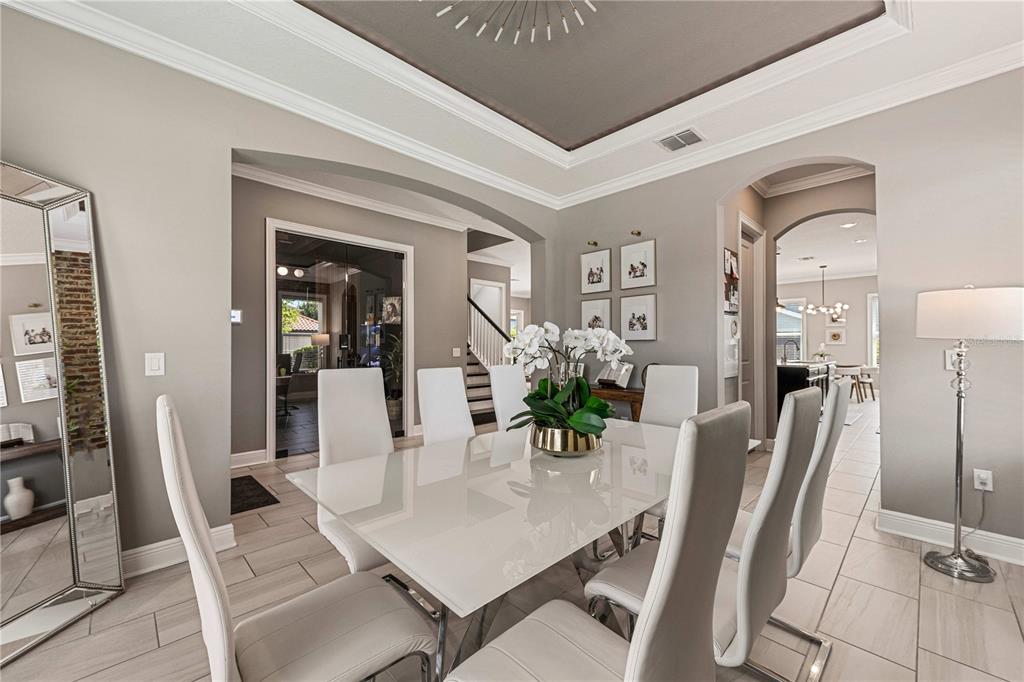 A modern dining room features a white table, six chairs, and a tray ceiling — 9225 HOLLISTON CREEK PLACE, WINTER GARDEN, FL