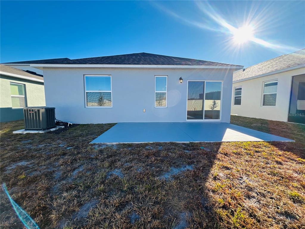 The back exterior of a house features a concrete patio, sliding glass doors, and windows — 3844 BLUETHREAD WAY, POINCIANA, FL