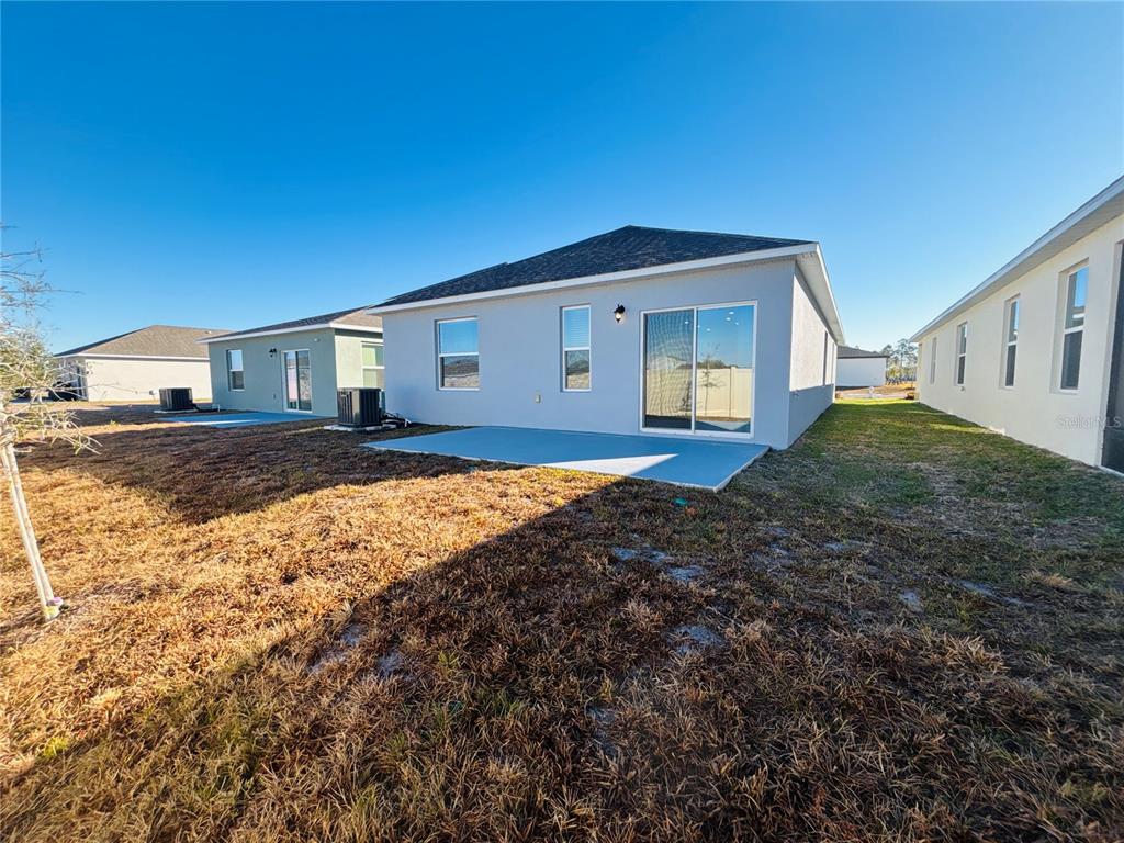 The rear exterior of a light gray house features a concrete patio and sliding doors — 3844 BLUETHREAD WAY, POINCIANA, FL