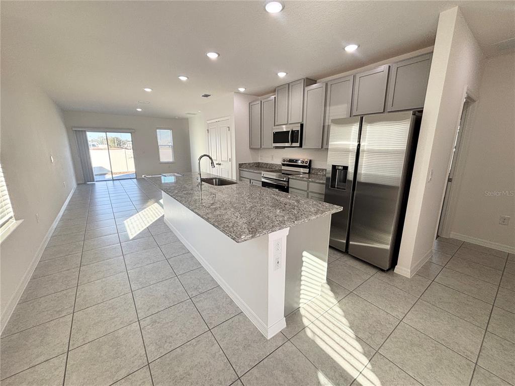 A kitchen features a granite-topped island, stainless steel appliances, and light gray cabinetry — 3844 BLUETHREAD WAY, POINCIANA, FL