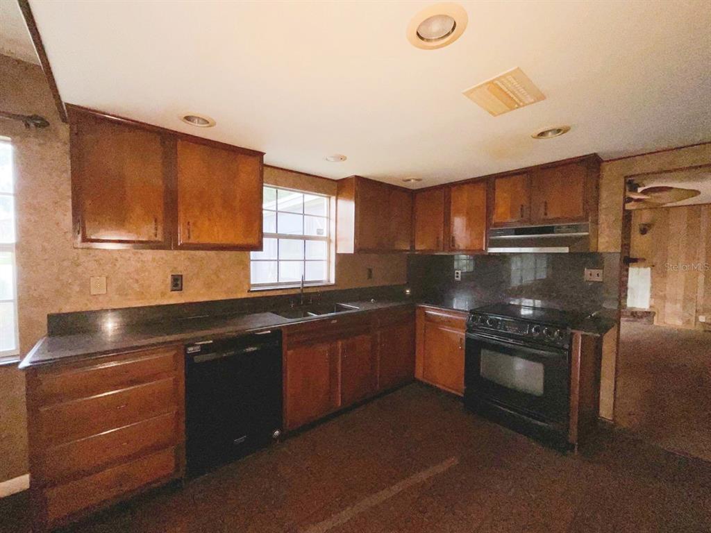 A kitchen with wood cabinets, dark countertops, a black dishwasher, and a black range — 603 W OCALA STREET, UMATILLA, FL