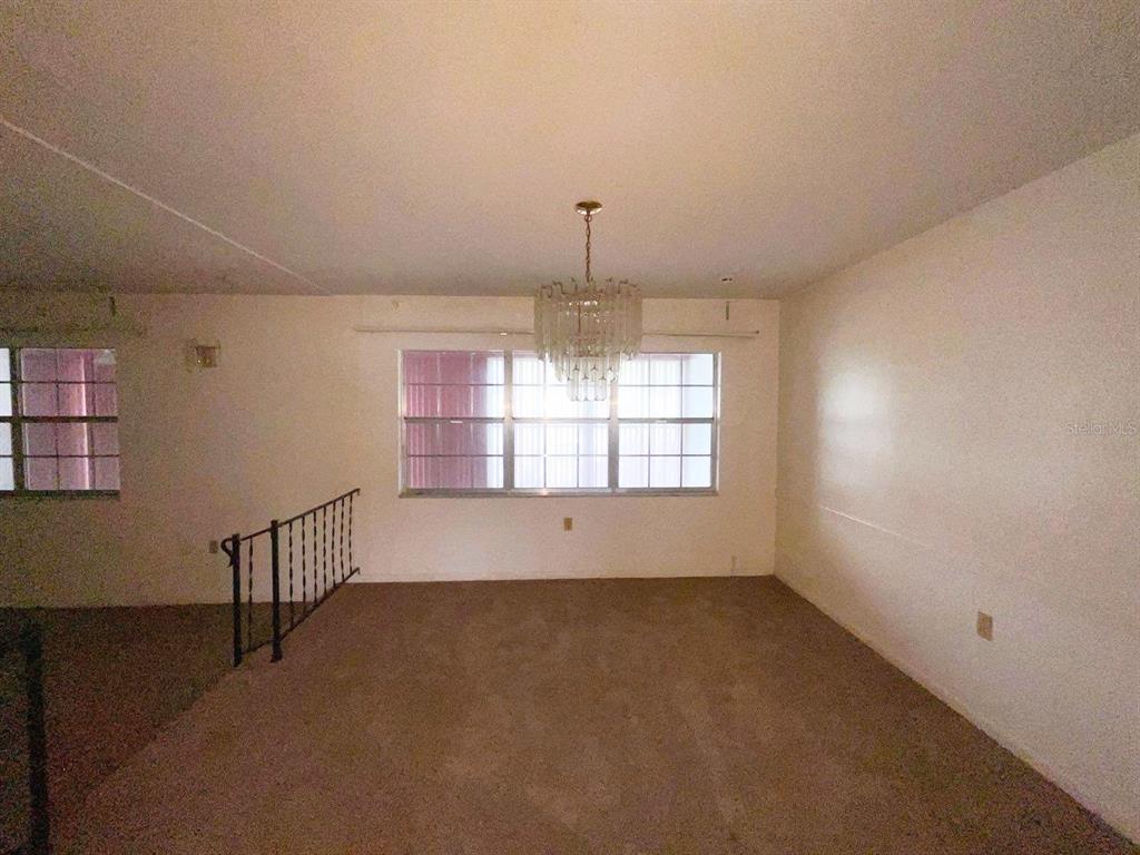 A carpeted room features a crystal chandelier, large windows, and a metal stair railing — 603 W OCALA STREET, UMATILLA, FL