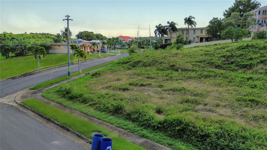A vacant, sloped grassy lot sits next to a paved road in a residential neighborhood — . HACIENDAS DE CAMUY, BO. PUENTE, SOLAR 11, CAMUY, PR