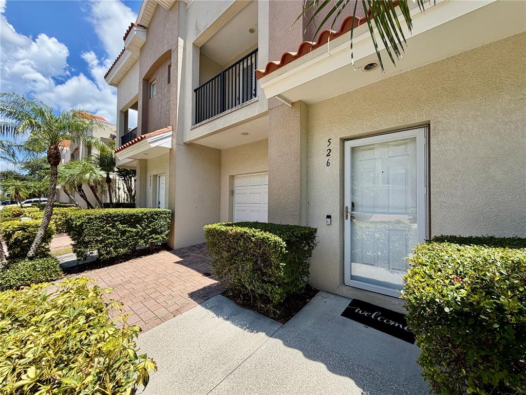 A two-story townhouse exterior features a white front door, a small garage, and landscaping — 526 101ST AVENUE N, ST PETERSBURG, FL