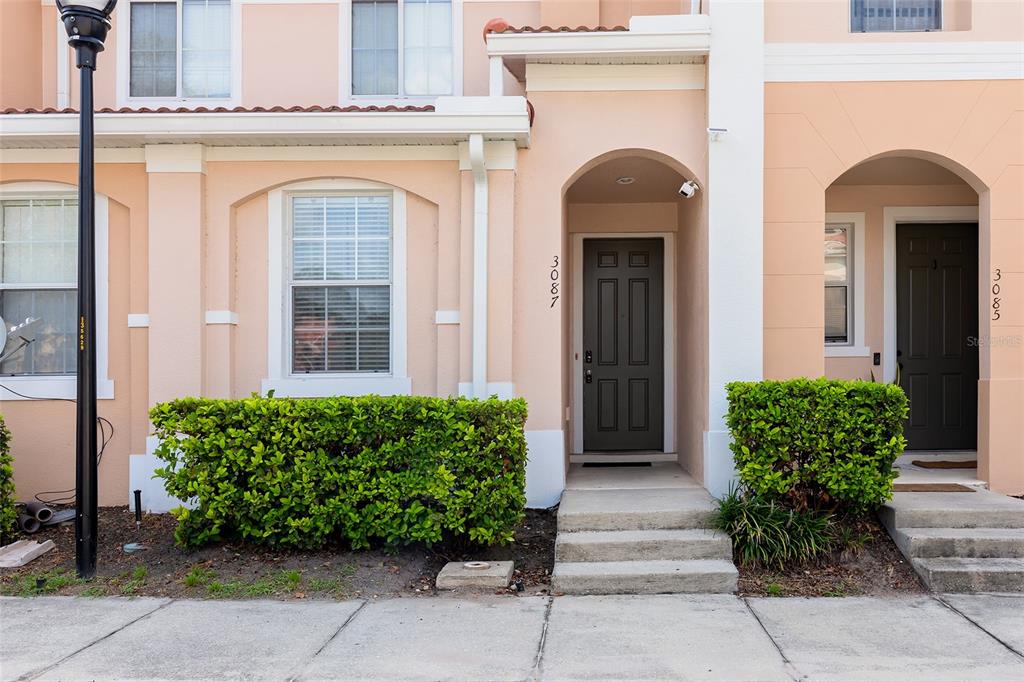 The exterior of two adjacent townhomes features peach-colored stucco walls, dark doors, and green hedges — 3087 SEAVIEW CASTLE DRIVE, KISSIMMEE, FL