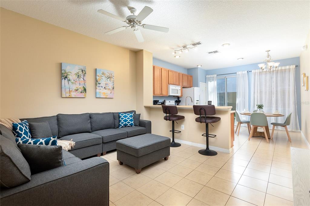 A living room with a gray sectional sofa opens to a kitchen and dining area — 3087 SEAVIEW CASTLE DRIVE, KISSIMMEE, FL