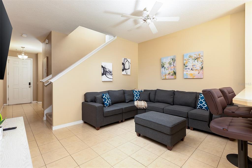 A living room features a large gray sectional sofa, a matching ottoman, and tile flooring — 3087 SEAVIEW CASTLE DRIVE, KISSIMMEE, FL