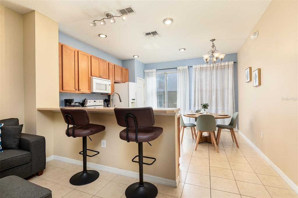 A kitchen with wood cabinets and a breakfast bar overlooks a dining area with chairs — 3087 SEAVIEW CASTLE DRIVE, KISSIMMEE, FL