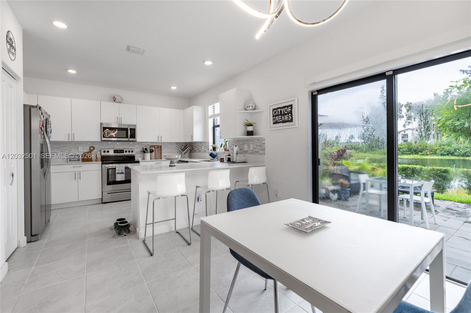 A modern kitchen features white cabinetry, stainless steel appliances, and a dining area overlooking a lake — 561 NW 204th St, Miami Gardens FL 33169, MIAMI GARDENS, FL
