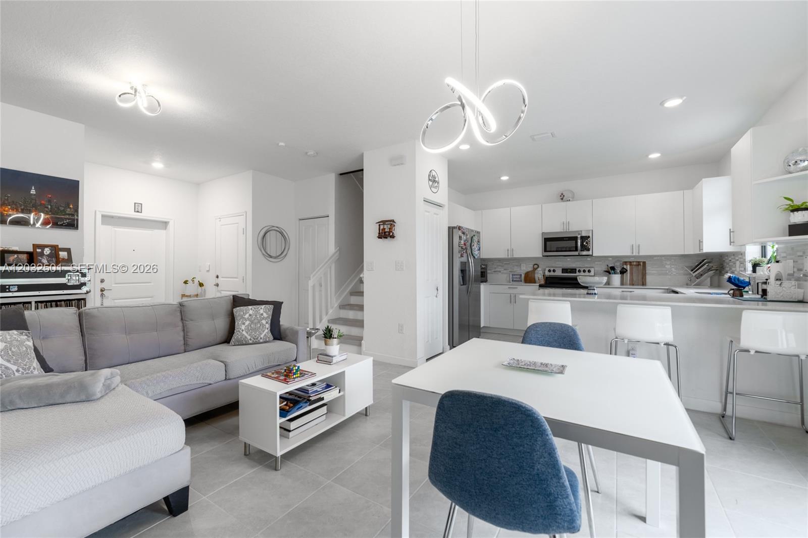 An open-concept living room and kitchen featuring white cabinetry, gray tile flooring, and stairs — 561 NW 204th St, Miami Gardens FL 33169, MIAMI GARDENS, FL