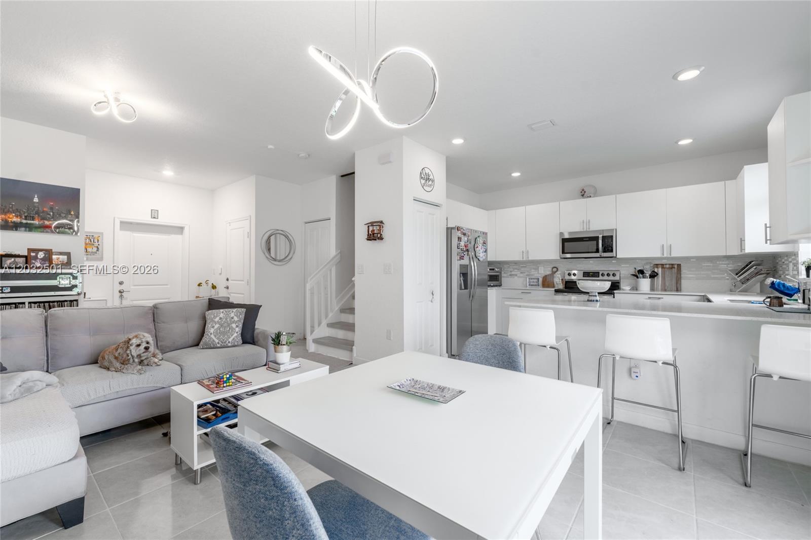An open-concept living and dining area features a modern kitchen, white cabinetry, and gray tile — 561 NW 204th St, Miami Gardens FL 33169, MIAMI GARDENS, FL