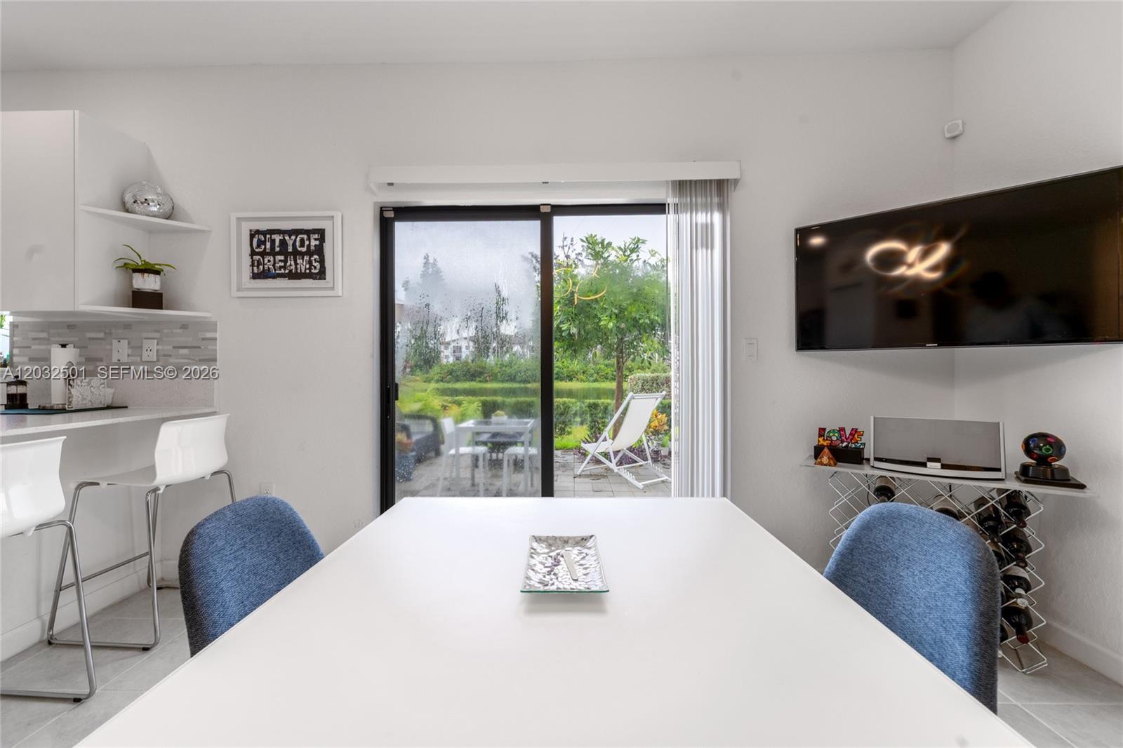 A dining area features a white table, blue chairs, a wall-mounted television, and sliding doors — 561 NW 204th St, Miami Gardens FL 33169, MIAMI GARDENS, FL