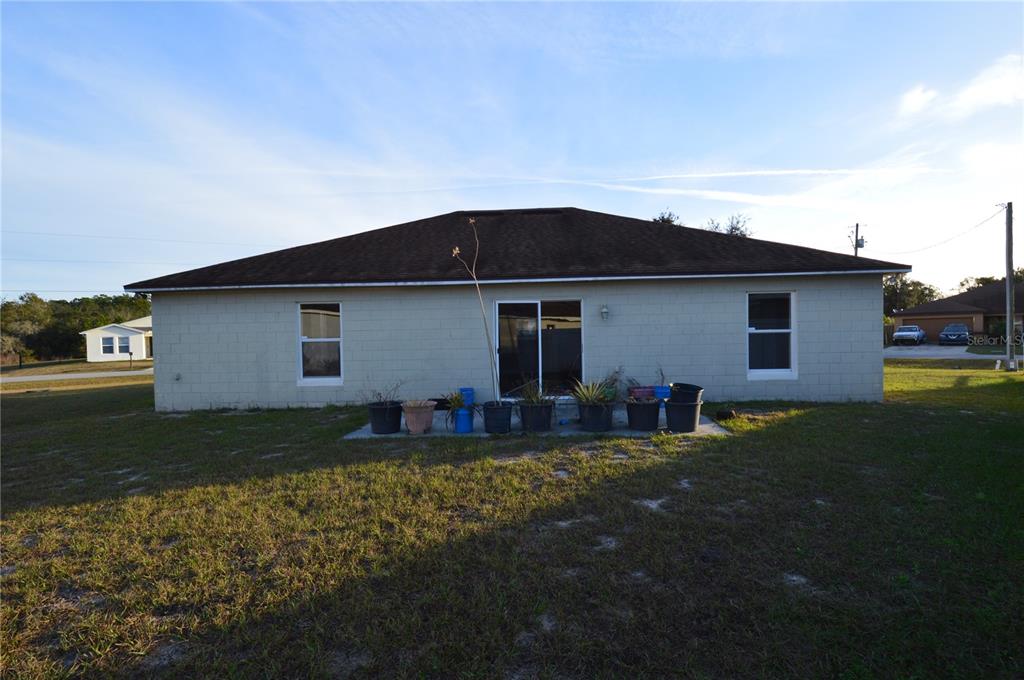 The rear exterior of a single-story concrete block house features a sliding glass door — 1617 PERDIDO COURT, KISSIMMEE, FL