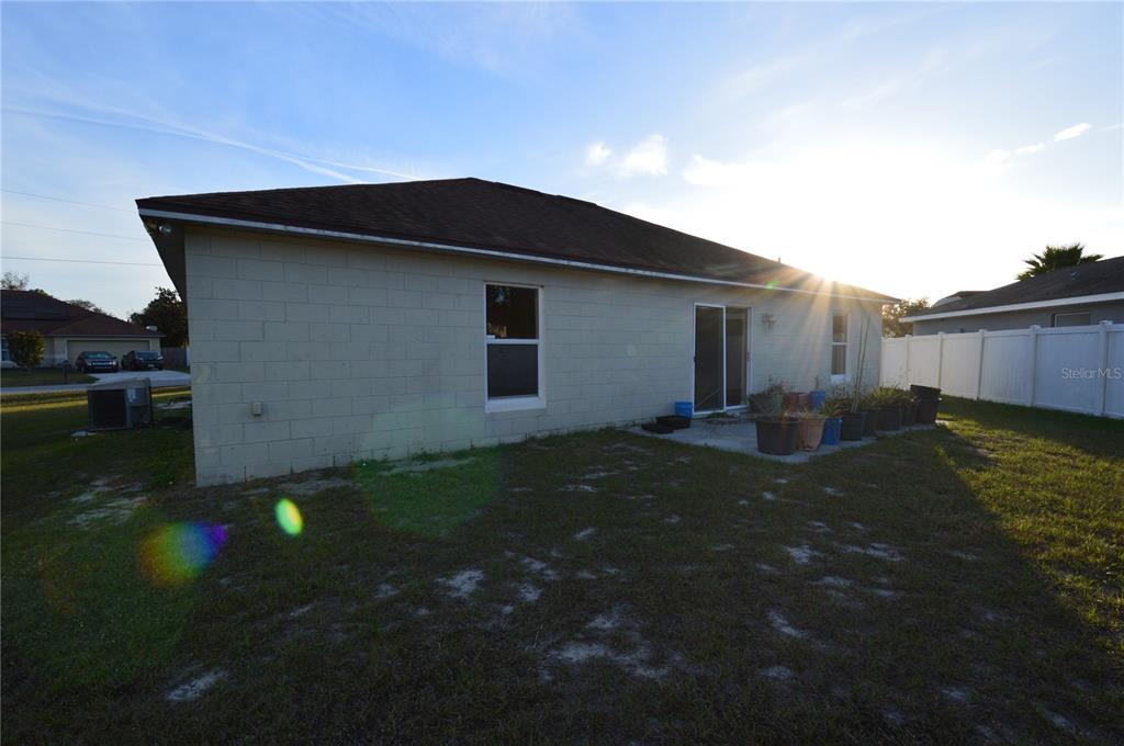 The exterior of a concrete block house features a sliding glass door and a small patio — 1617 PERDIDO COURT, KISSIMMEE, FL