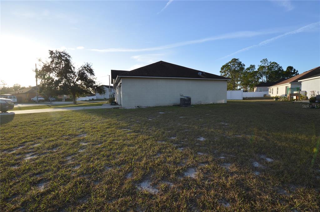 A side view of a house exterior with a large grassy yard and an air conditioner — 1617 PERDIDO COURT, KISSIMMEE, FL