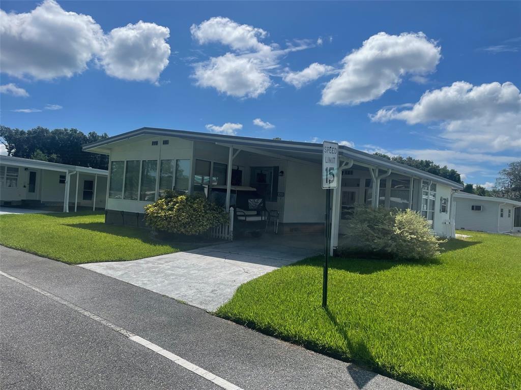 A single-story manufactured home features a carport, a concrete driveway, and a speed limit sign — 408 HAWTHORNE BOULEVARD, LEESBURG, FL