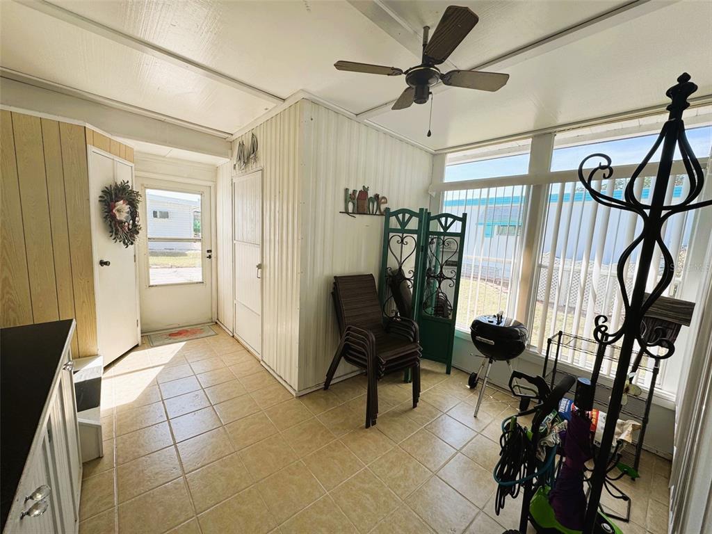 A sunroom features tiled flooring, a ceiling fan, and large windows overlooking a neighboring home — 408 HAWTHORNE BOULEVARD, LEESBURG, FL
