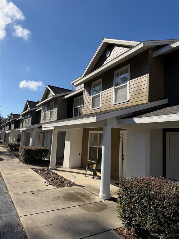 A row of multi-story townhomes with tan siding, white columns, and concrete walkways — 2306 SW 42ND DRIVE UNIT 140, GAINESVILLE, FL