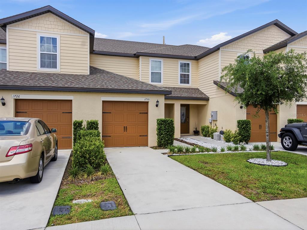 A row of townhouses with tan siding, brown garage doors, and concrete driveways — 1730 WYNFORD CIRCLE, TAVARES, FL
