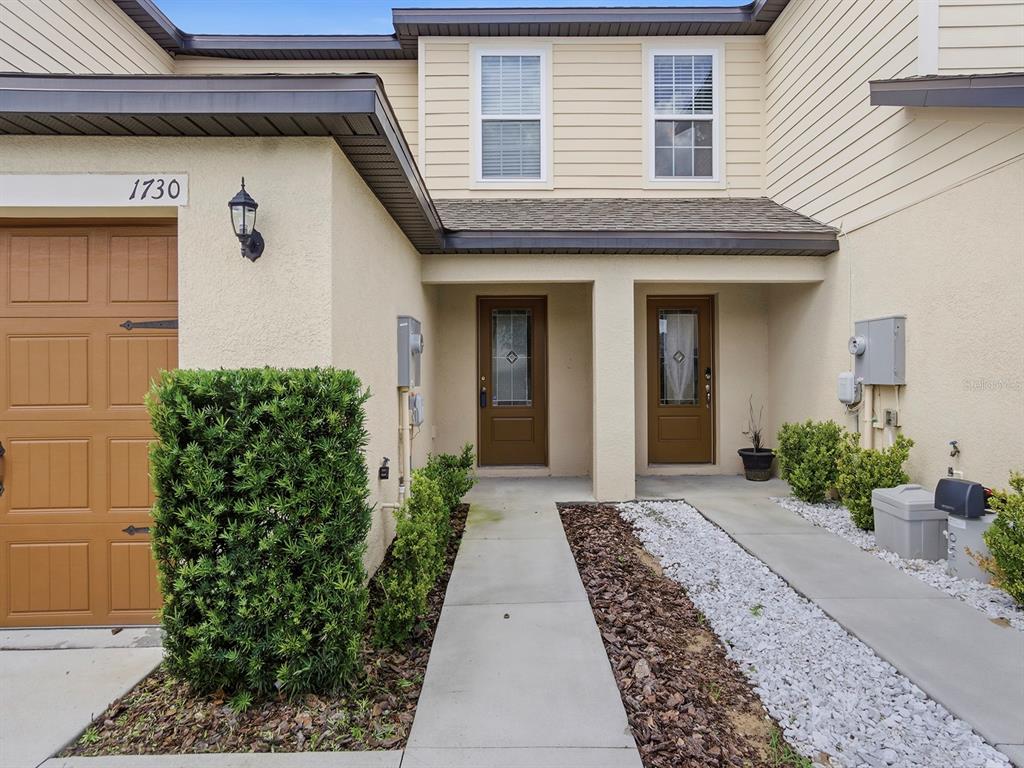 A two-story townhouse exterior features a garage, two front doors, and a concrete walkway — 1730 WYNFORD CIRCLE, TAVARES, FL