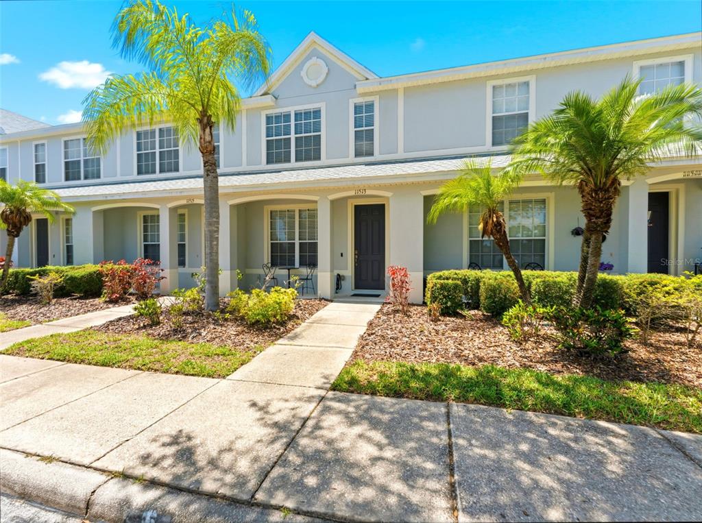 A two-story townhouse exterior features light-colored siding, arched entryways, and palm trees in front — 11513 DECLARATION DRIVE, TAMPA, FL