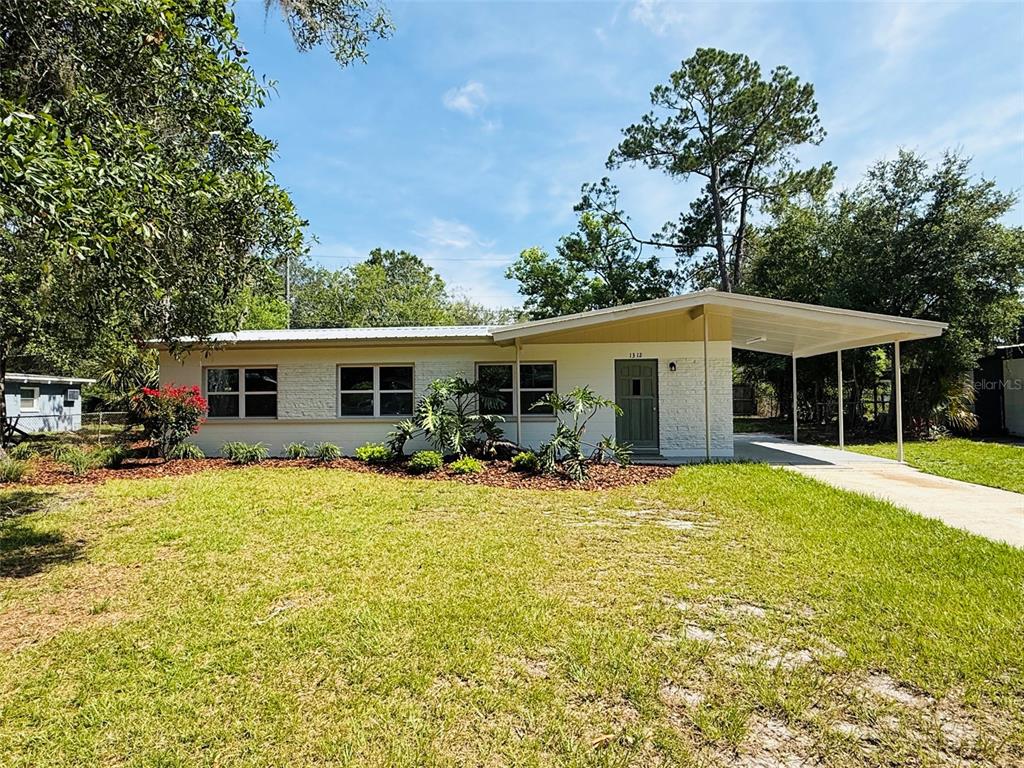 A single-story white brick house features a front carport and a green front door — 1312 NE 28TH AVENUE, GAINESVILLE, FL