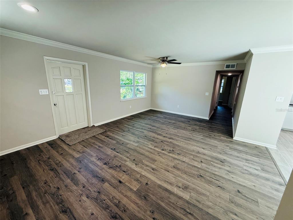 An empty living room features light gray walls, crown molding, and dark wood-look flooring — 1312 NE 28TH AVENUE, GAINESVILLE, FL