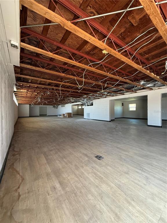 An open-concept commercial space features exposed wooden ceiling beams and light-colored wood-look flooring — 109 W BRIDGERS AVENUE, AUBURNDALE, FL