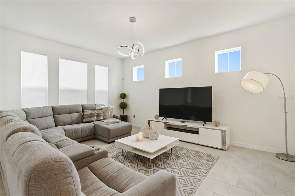 A modern living room features a gray sectional sofa, white media console, and geometric chandelier — 2800 CELLO LANE, KISSIMMEE, FL