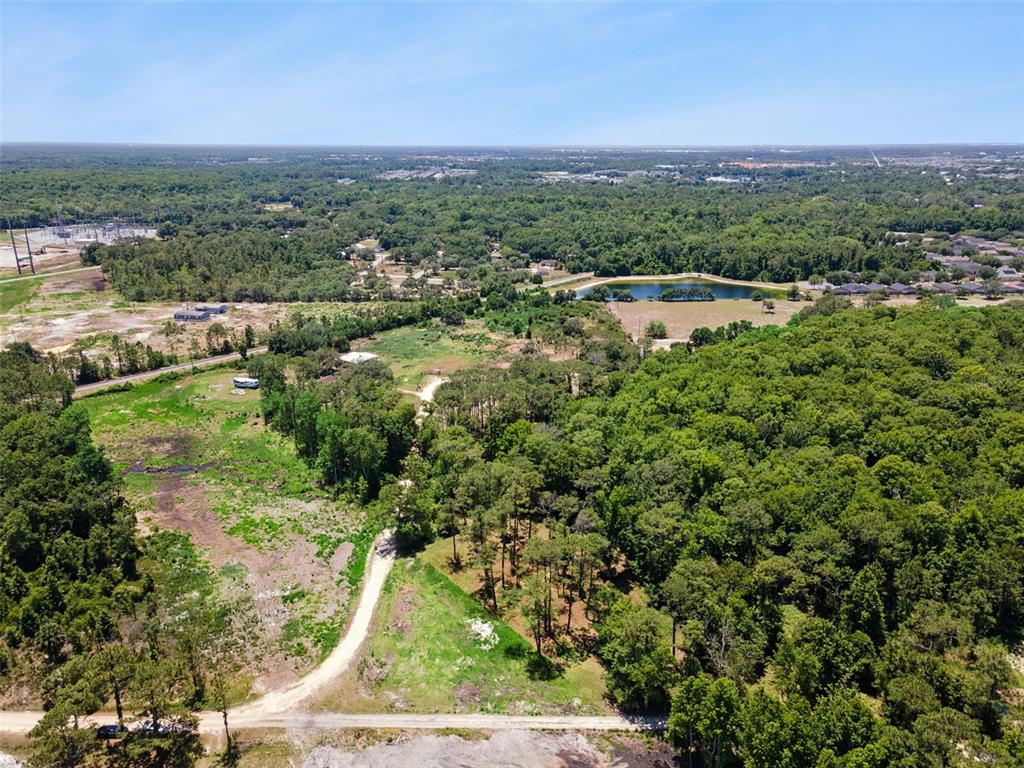An aerial view shows a dirt road leading through a wooded lot with a pond — STATE ROAD 532, DAVENPORT, FL