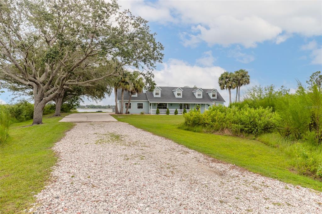 A light blue house with a gravel driveway sits on a grassy lot with trees — 2018 MONTERO CIRCLE, DELTONA, FL