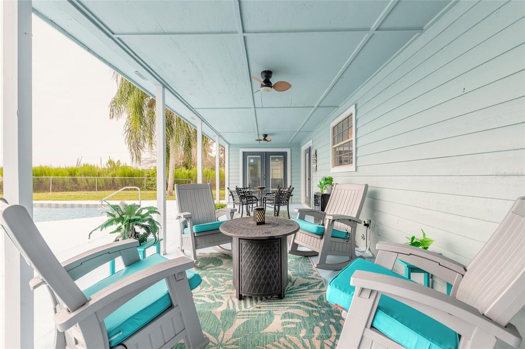 A covered patio features light blue siding, rocking chairs, a fire pit, and a pool view — 2018 MONTERO CIRCLE, DELTONA, FL