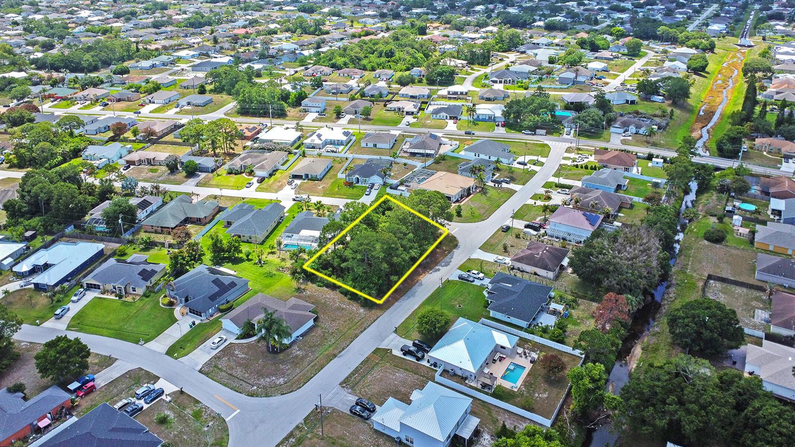An aerial view shows a vacant, tree-covered residential lot outlined in yellow within a neighborhood — 1399 SW Halford Avenue, FL 34953, FL