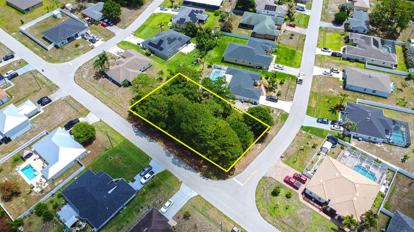 An aerial view shows a vacant, tree-covered residential lot outlined in yellow between two streets — 1399 SW Halford Avenue, FL 34953, FL