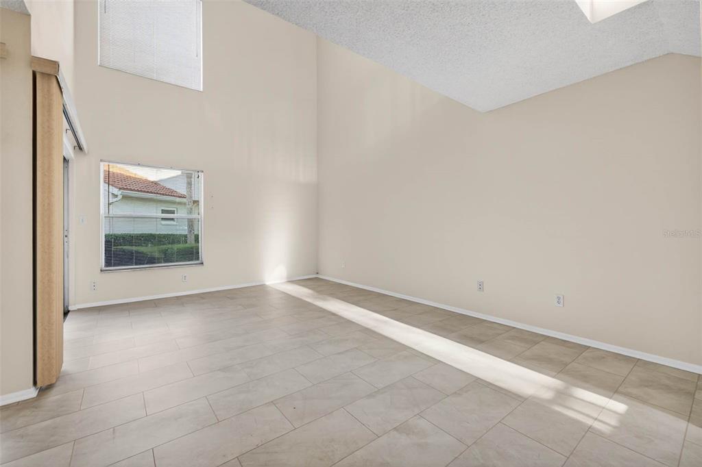 An empty room with high ceilings, light-colored tile flooring, and a sliding glass door — 4843 NAPOLI COURT NE, ST PETERSBURG, FL