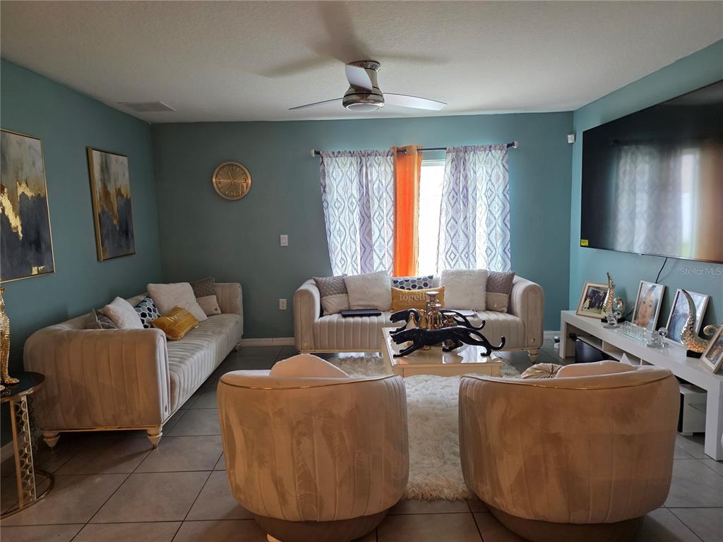 A living room features two beige sofas, two matching armchairs, and a large wall-mounted television — 566 SUNLIT CORAL STREET, RUSKIN, FL