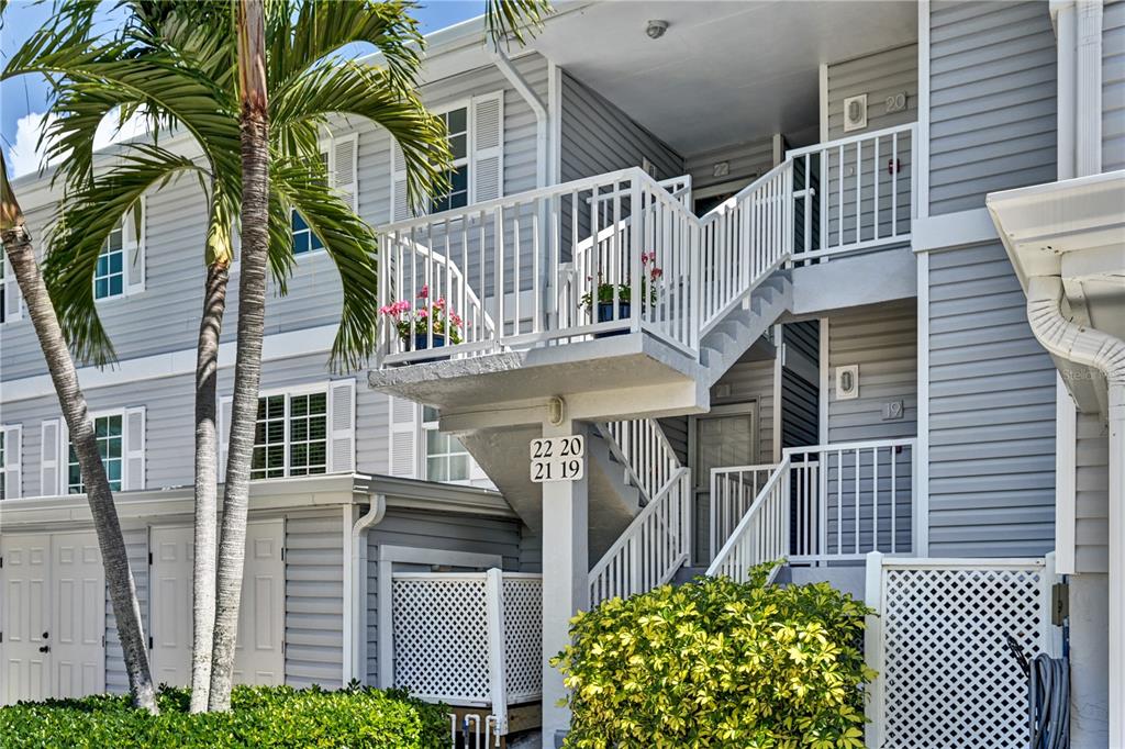 An exterior view of a multi-story apartment building with stairs, balconies, and palm trees — 5854 GASPARILLA ROAD UNIT M22, BOCA GRANDE, FL