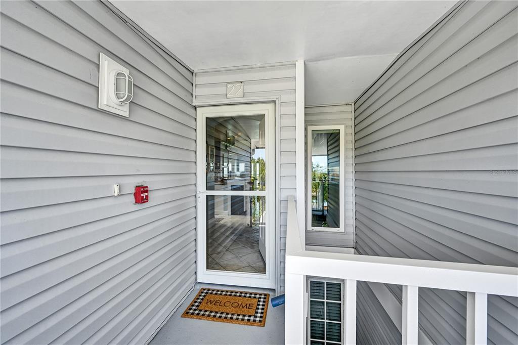 A gray-sided exterior entryway features a white storm door, a welcome mat, and a railing — 5854 GASPARILLA ROAD UNIT M22, BOCA GRANDE, FL