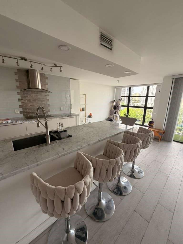 A modern kitchen features a marble island with four bar stools and a tile backsplash — 400 Leslie Dr # 508, Hallandale Beach FL 33009, HALLANDALE BEACH, FL