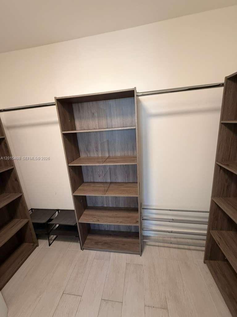A walk-in closet features wood-grain shelving units and metal clothing rods against white walls — 400 Leslie Dr # 508, Hallandale Beach FL 33009, HALLANDALE BEACH, FL