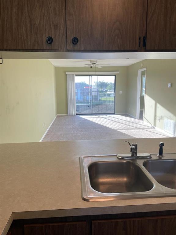 A kitchen sink and countertop overlook a living area with a sliding glass door — 39132 COUNTY ROAD 54 UNIT 2084, ZEPHYRHILLS, FL