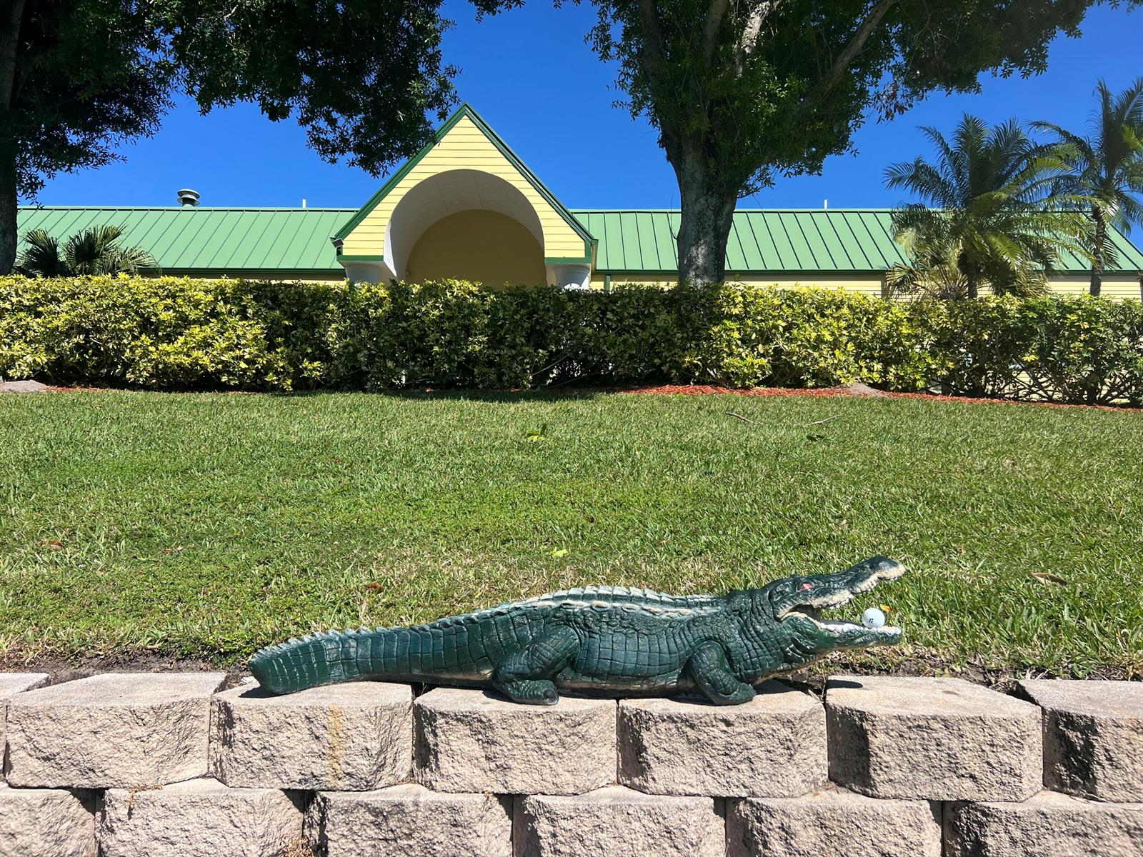 A green alligator statue holding a golf ball sits on a stone wall before a building — 4310 Gator Trace Circle, Fort Pierce FL 34982, FORT PIERCE, FL